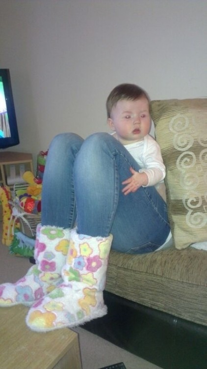Una bebé sentada en un sillón donde parece tener piernas de mujer 