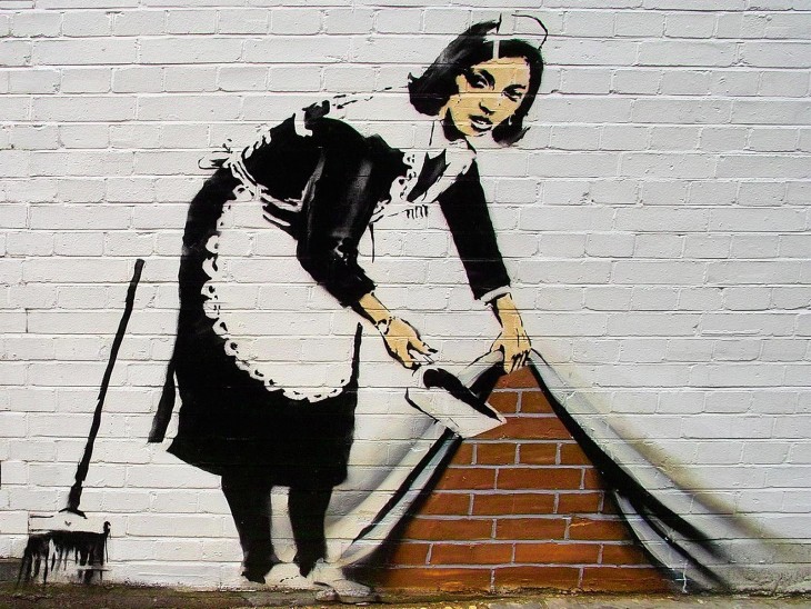 Grafiti de Bansky que muestra una mujer levantando una cortina y echando basura dentro 