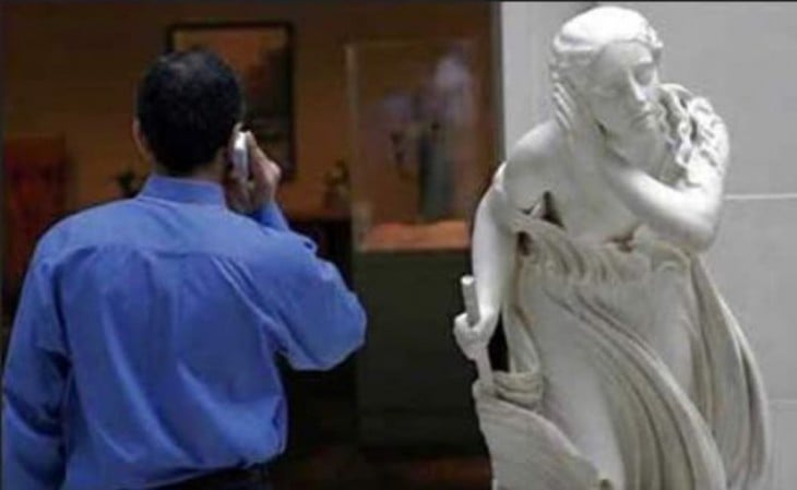 foto de un hombre hablando por teléfono a un lado de una estatua que parece que lo va a escuchar 