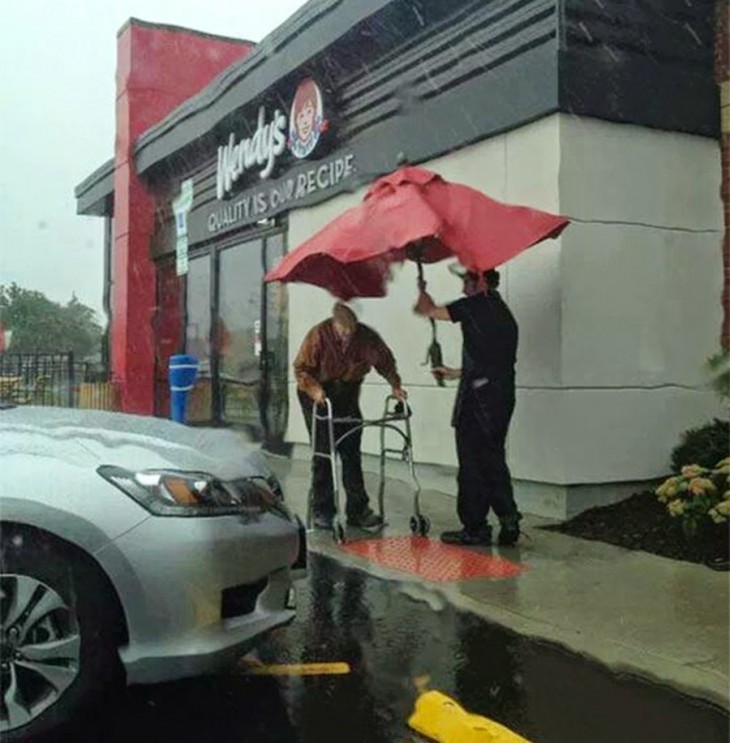 joven trabajador del wendys le ayuda a un anciano a caminar mientras llueve intenta cubrirlo