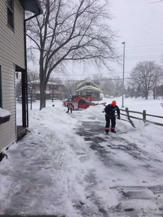 rescatistas ayudando a un anciano a quitar la nieve de su porche mientras él se encuentra en recuperacióm