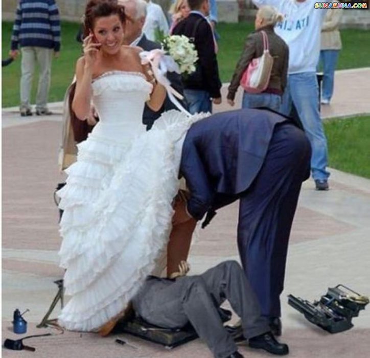 dos hombres viendo algo abajo del vestido de novia de la chica